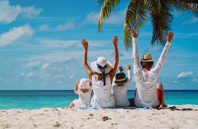 A family of four raising hands while sitting on the shore of the beach.